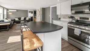 A modern kitchen with a central island, stainless steel appliances, and a seating area with a sofa and chairs. - The Salty Oyster - Amazing Deck and Short Walk to beach! (Hampton)