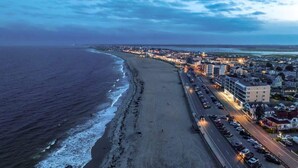 A coastal cityscape with a beach, a road lined with buildings, and a clear sky. - The Fleet -  Perfect Location Near Beach & Boardwalk (Hampton)
