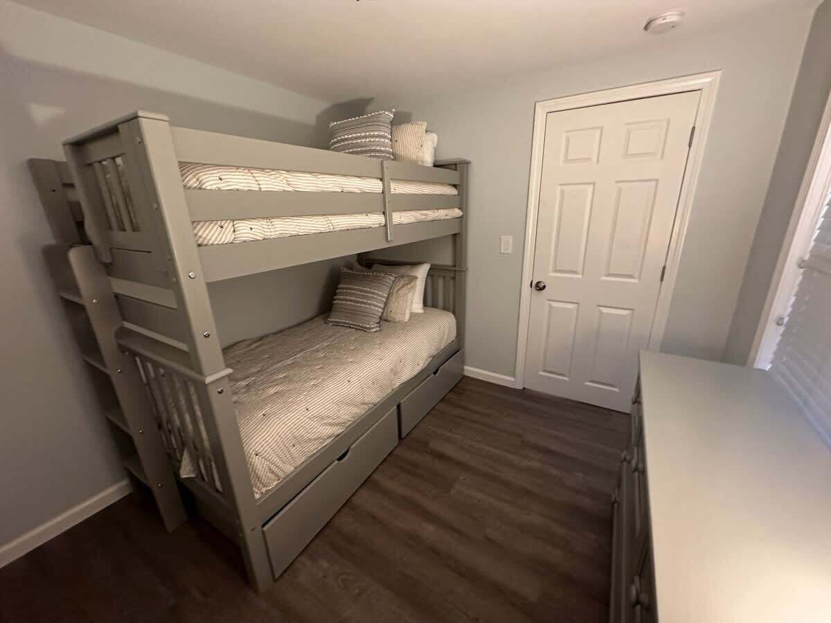 Una cama litera con cajones de almacenamiento, una puerta blanca y piso de madera.