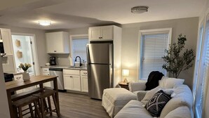 A compact living space with a kitchenette, a dining area, and a seating area with a sofa and cushions. - Riptide Retreat - Walk to Hampton & Seabrook Beach! (Seabrook)