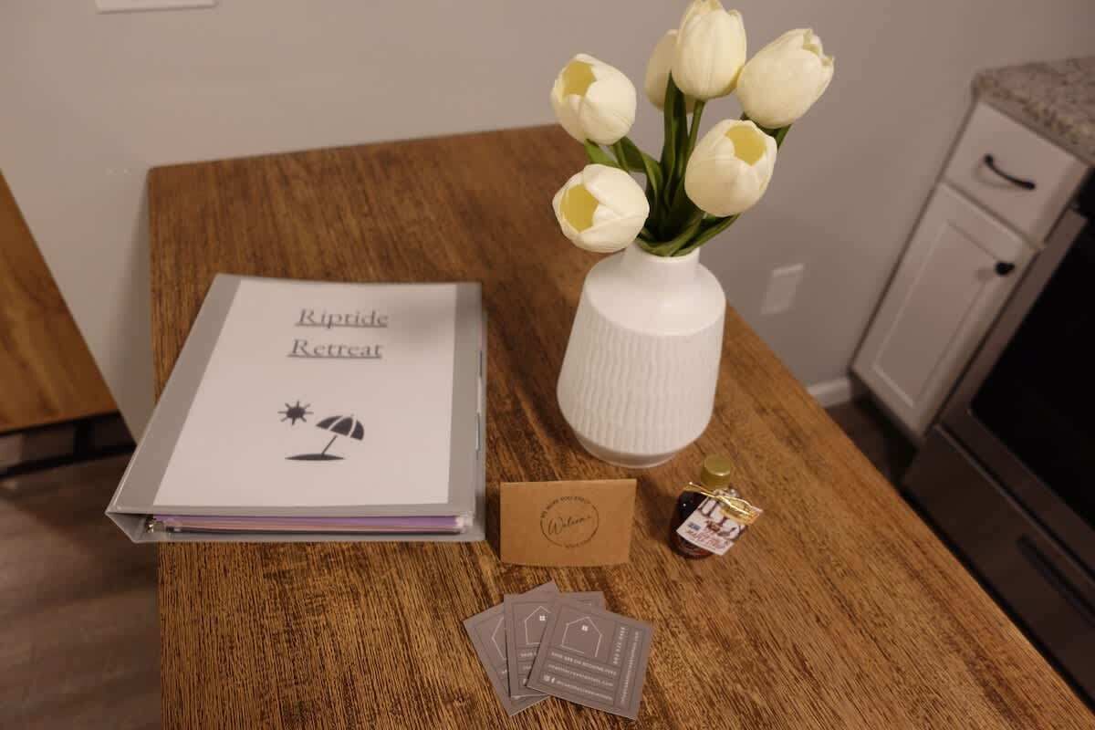 Une table en bois sur laquelle se trouve un vase blanc rempli de tulipes, une brochure intitulée « Kipride Retreat », une petite boîte marron et quelques dépliants.