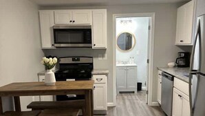 A modern kitchen with white cabinets, a wooden table, and a stainless steel refrigerator. - Riptide Retreat - Walk to Hampton & Seabrook Beach! (Seabrook)