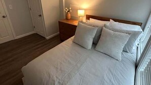 Un dormitorio con cama, mesita de noche, lámpara y una puerta.