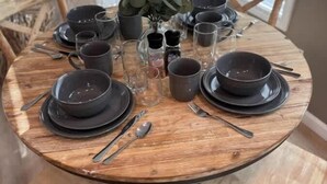 Una mesa de madera redonda dispuesta con platos, tazones, vasos y cubiertos.