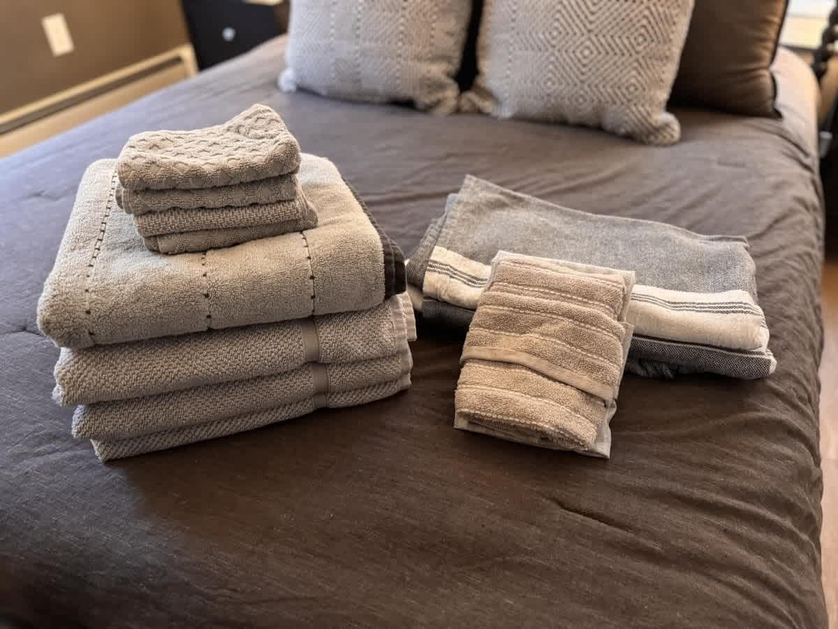 A neatly arranged stack of folded towels on a bed with a dark brown cover.