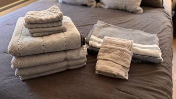 A neatly arranged stack of folded towels on a bed with a dark brown cover.