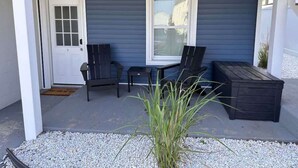 Un patio couvert avec une porte, deux chaises, une table et un jardinière.