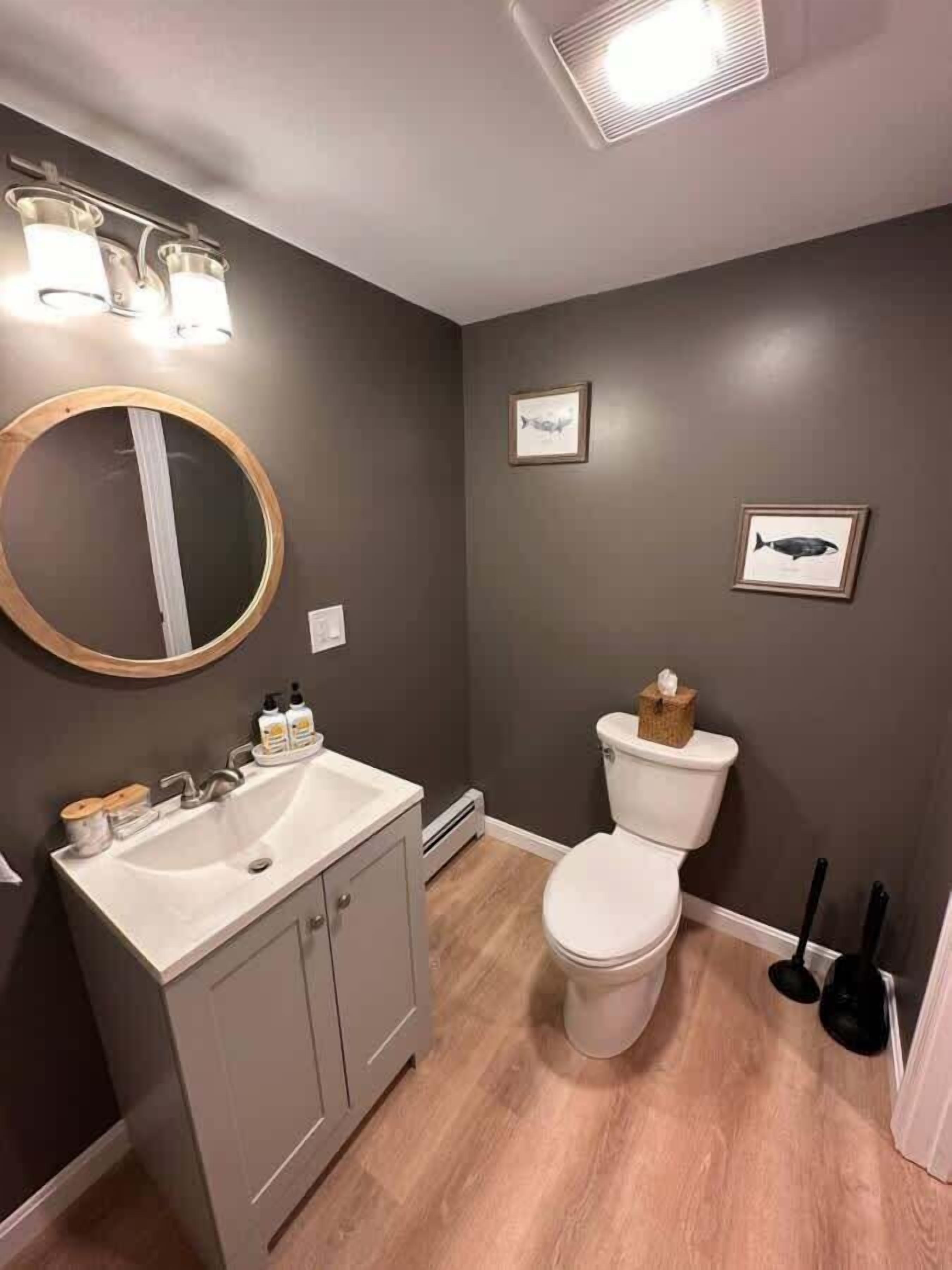 Une salle de bain équipée d’un lavabo, d’un miroir, de toilettes et de tableaux représentant des poissons, accrochés au mur.