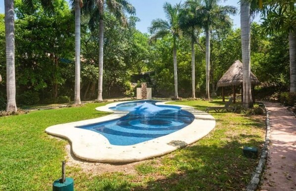 Une piscine à la forme originale, entourée de palmiers et abritée par une structure à toit de chaume.