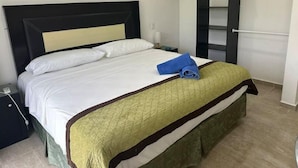 A neatly made bed with white linens and a green quilted bedspread, a blue towel on the bed, and a black headboard.