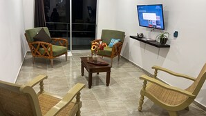 Un área de espera con sillones de mimbre, una mesa de centro de madera con un florero y un televisor de pantalla plana montado en la pared.