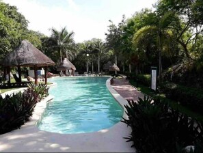 A swimming pool surrounded by lush greenery and thatched-roof structures.