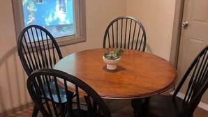 A dining area with a round wooden table, six black chairs, a white pendant light, and a window with blinds. - Hidden Cottage Wooded Escape 2 bed/1 bath (Johnson City)