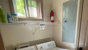A laundry area with a washer and dryer, a window, a fire extinguisher, and a door. - Hidden Cottage Wooded Escape 2 bed/1 bath (Johnson City)