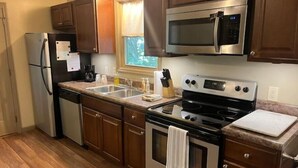A kitchen with wooden cabinets, stainless steel appliances, a double sink, and a window providing natural light. - Hidden Cottage Wooded Escape 2 bed/1 bath (Johnson City)