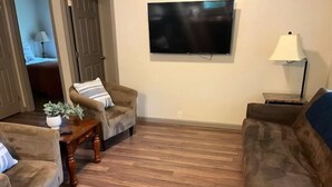 A living room with a wooden floor, two sofas, a coffee table, a TV mounted on the wall, and a lamp. - Hidden Cottage Wooded Escape 2 bed/1 bath (Johnson City)