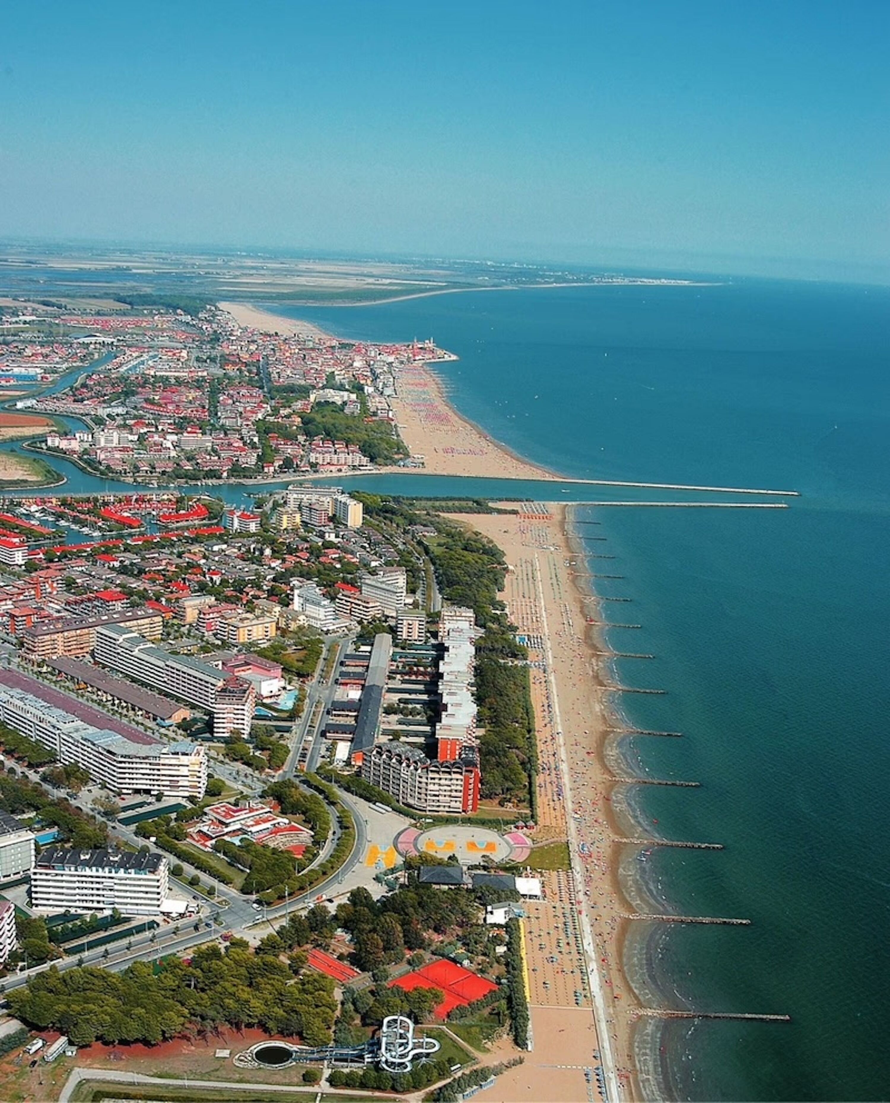 An aerial view of a coastal city with a beach, residential areas, and a sports complex.