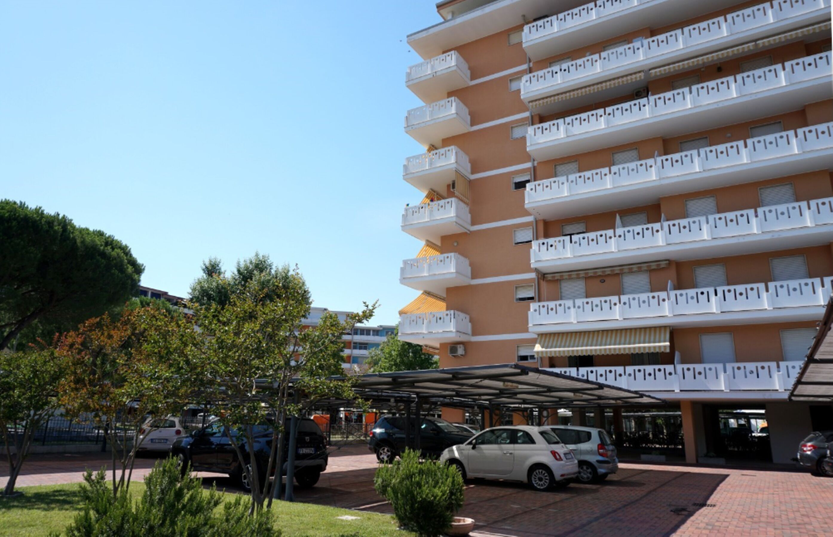 A multi-story hotel with balconies, a covered parking area, and a landscaped garden.