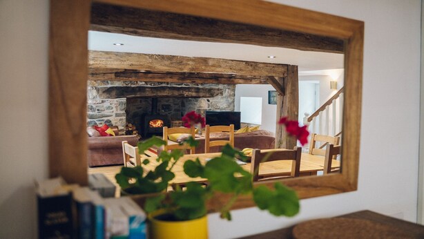 A living room with a stone fireplace, wooden beams, and a mirror reflecting the space.