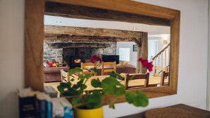 Una sala de estar con chimenea de piedra, vigas de madera y un espejo que refleja el espacio.