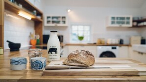 A kitchen counter with a loaf of bread, a knife, a milk bottle, and two patterned cups.