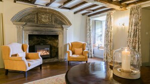 Una habitación acogedora con chimenea, dos sillones, una mesa con una vela y una ventana con cortinas.