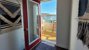 A hallway with a red door leading to a balcony with a view of a body of water and hills. - The Battery Harbour Home, Ocean&City View,Parking (St. John's)