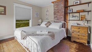 Ein Schlafzimmer mit Bett, Kommode, Fenster und einer Ziegelwand.