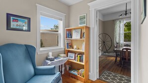 Ein gemütliches Zimmer mit einem blauen Sessel, einem Holzregal und einer Essecke mit Tisch und Stühlen.