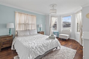 Un dormitorio con una cama grande, dos mesitas de noche, una silla y vistas al exterior.