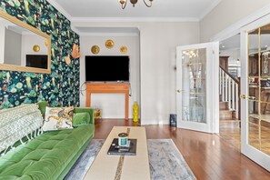 Una sala de estar con un sofá verde, un televisor de pantalla plana, una chimenea y una escalera que sube a otro nivel.