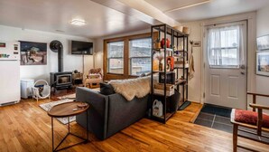 A cozy living room with a sofa, a TV, a fireplace, and a bookshelf. - Iconic Battery Cottage Signal Hill Sea&City Views (St. John's)
