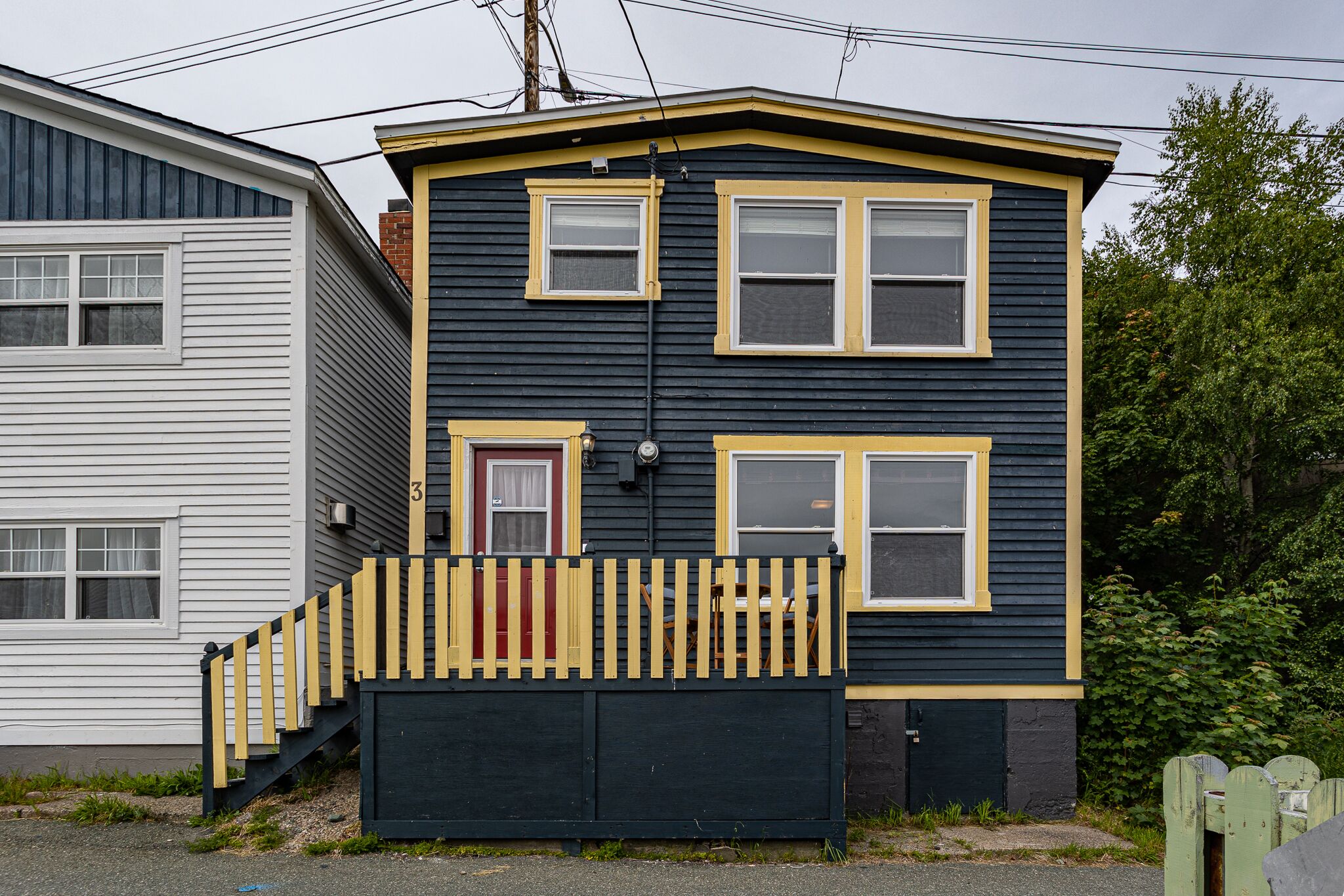 A two-story house with a wooden staircase leading to the front door, a small porch, and a fenced yard.