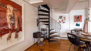 A modern interior with a spiral staircase, a large abstract painting, and a dining area with a round table. - Iconic Battery Cottage Signal Hill Sea&City Views (St. John's)