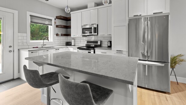 Una cocina moderna con armarios blancos, electrodomésticos de acero inoxidable y una isla central con taburetes de bar.