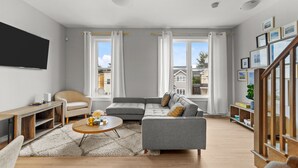 Una sala de estar moderna con un sofá seccional gris, una mesa redonda, un mueble bajo para la televisión de madera y una estantería.