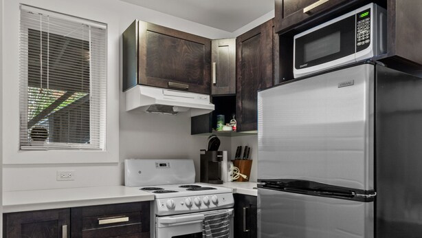 A modern kitchen with dark wooden cabinets, stainless steel appliances, and a window with blinds.