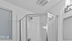 A modern bathroom with a glass-enclosed shower, a white toilet, a vanity with drawers, and a small shelf with toiletries.