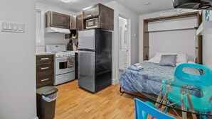 A compact kitchen with a refrigerator, stove, microwave, and a small trash bin.