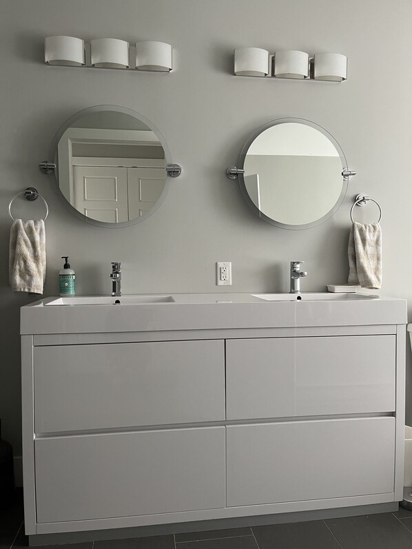 Une salle de bain moderne avec deux vasques, un grand miroir et des luminaires fixés au mur.