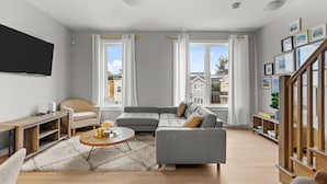 A modern living room with a grey sectional sofa, a round coffee table, a wooden TV stand, and a bookshelf.