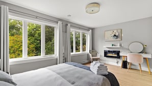A bedroom with a bed, a desk, a chair, a fireplace, and large windows.