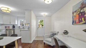 A modern kitchen with white cabinets, a dining area with a white table, and a painting of colorful buildings on the wall.