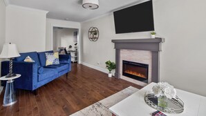 A living room with a blue sofa, a fireplace, a flat-screen TV, and a modern lamp.