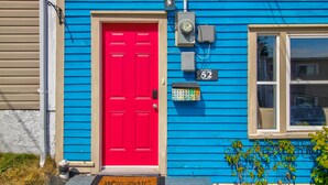A blue house with a red door, a welcome mat, and a street sign.