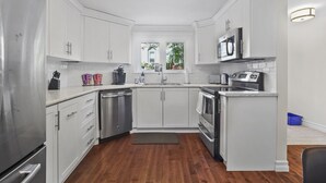 A modern kitchen with white cabinets, stainless steel appliances, and a wooden floor.
