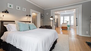Ein Schlafzimmer mit einem großen Bett, einem Schreibtisch und einem Sessel. Eine Tür führt in einen anderen Raum.