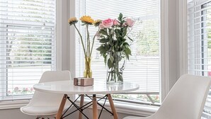 Ein runder Tisch mit zwei weißen Stühlen, einer Vase mit rosa Blumen und einer Vase mit gelben Blumen.