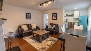 A modern living room with two leather sofas, a wooden coffee table, and a dining table with chairs. A kitchen with a blue refrigerator is visible in the background. - The Bannerman Park Loft Private Parking King Bed (St. John's)
