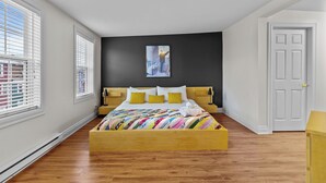 Un dormitorio con cama de madera, paredes blancas, una pared de acento negra y una ventana con persianas.